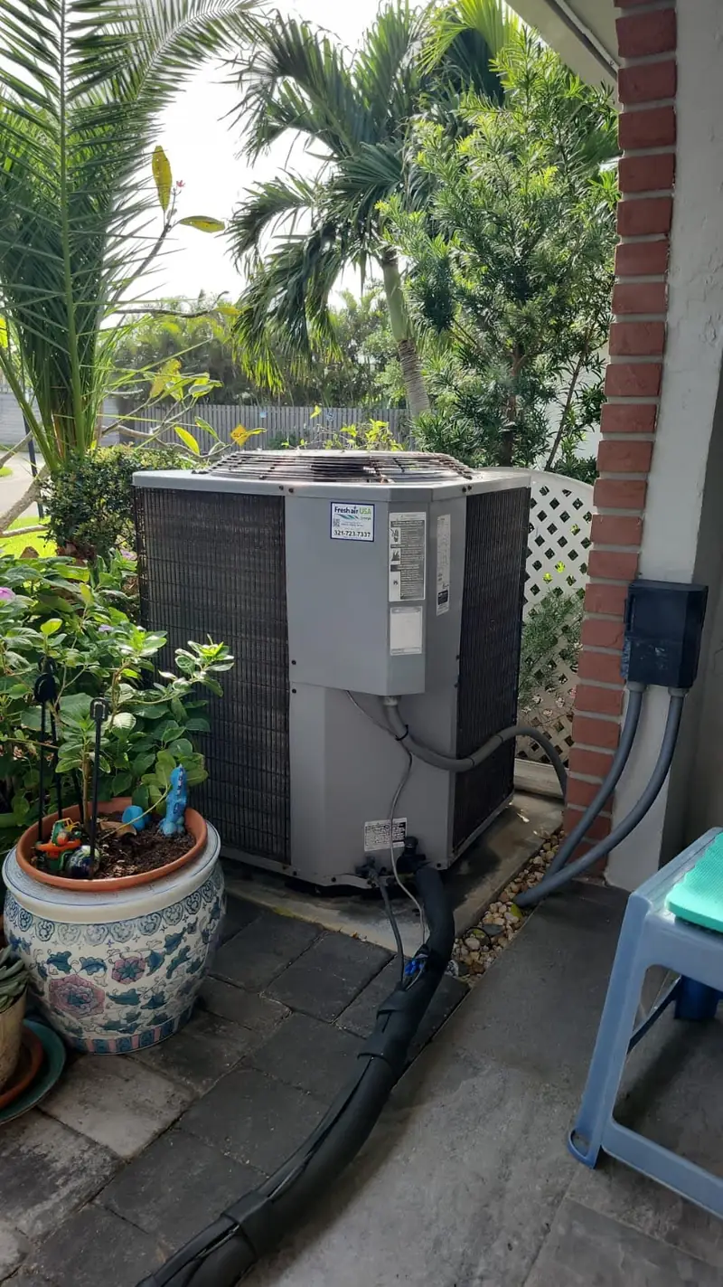 Residential condenser installed beside a planted patio
