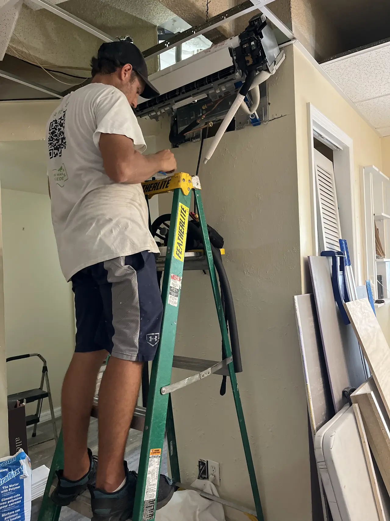 Technician on a ladder fitting an indoor air handler